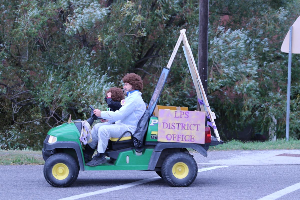 District business manager Peter Grady drives the Bob Ross-themed float for the District Office, whose staff all donned fluffy brown wigs.