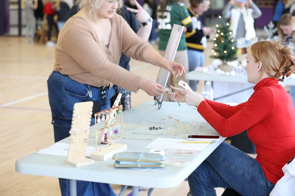 Kiersten Tobias exchanges business with Jasmine Anderson at her jewelry booth on market day.