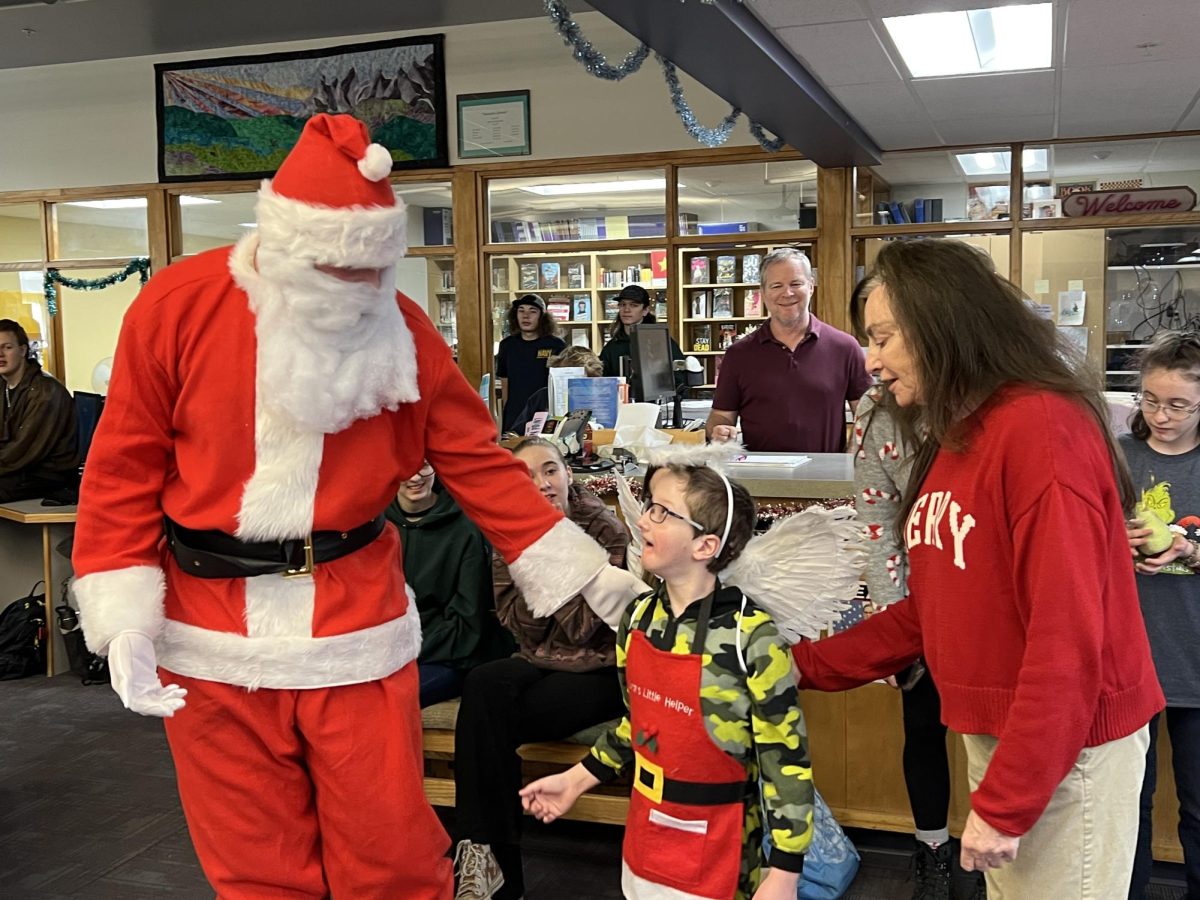 During the AP Lit play, Lliam Edwards as Santa Claus directs a middle school student towards the Christmas tree, while play director Carol Powalisz stands at his side.