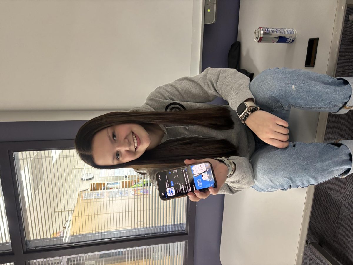Senior Maddie Wise holds up the app that will be used to track players and hold information on senior assassin. 